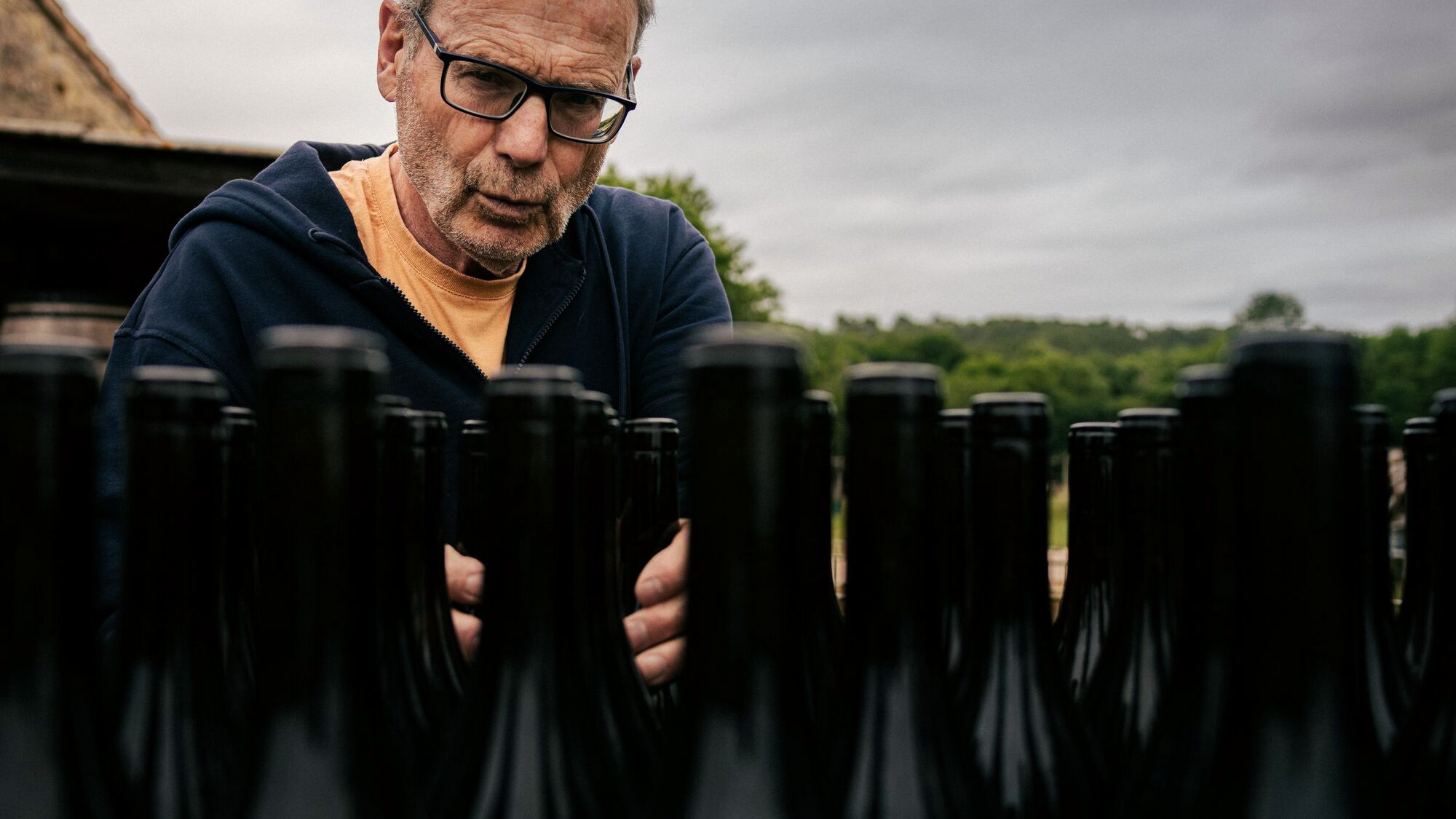 A winemaker carefully inspecting a row of bottles outdoors.